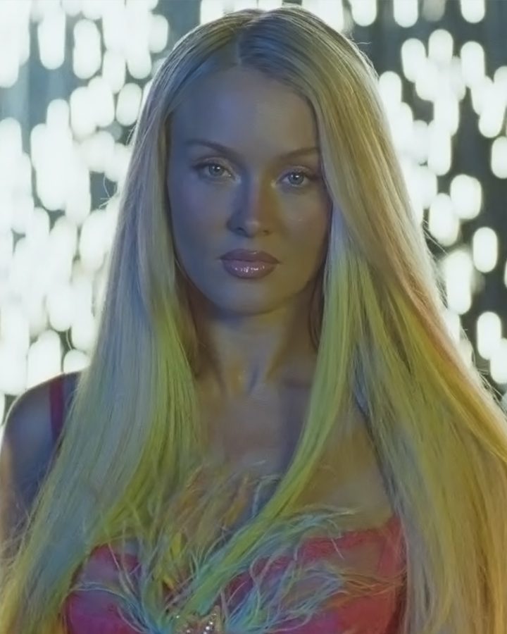 Zara Larrson in soft glam makeup facing the camera against a background of falling sparks